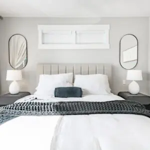 Bedroom with a bed, pillows, and a blanket, two lamps on the bedside tables, two mirrors on the wall