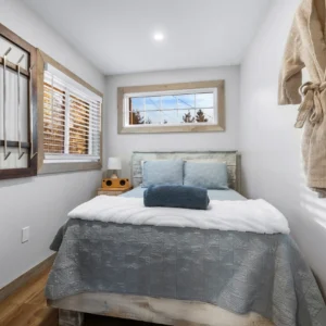 Bedroom with a bed, pillows, blanket and cushions, a dress hung on the wall, a lamp